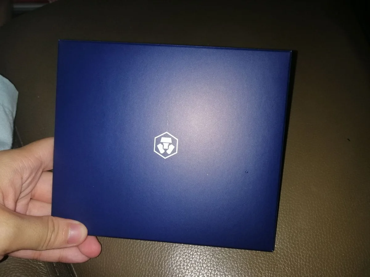 My hand holding the dark blue box of a Crypto.com MCO Visa card, in March 2020.