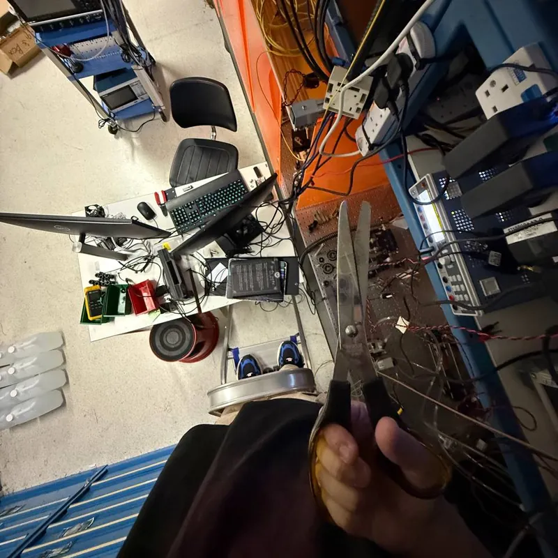 Looking down from the top of a ladder at the lab floor and a desk, holding a pair of scissors next to a rack of cables.