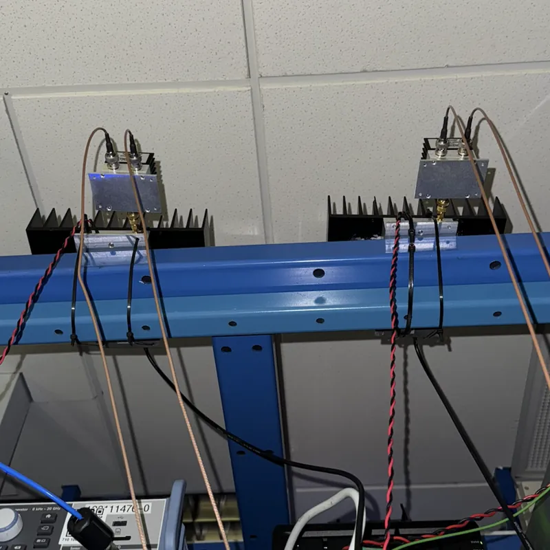 Two RF amplifiers with black finned heatsinks, cable-tied to a blue rack above the optical table.